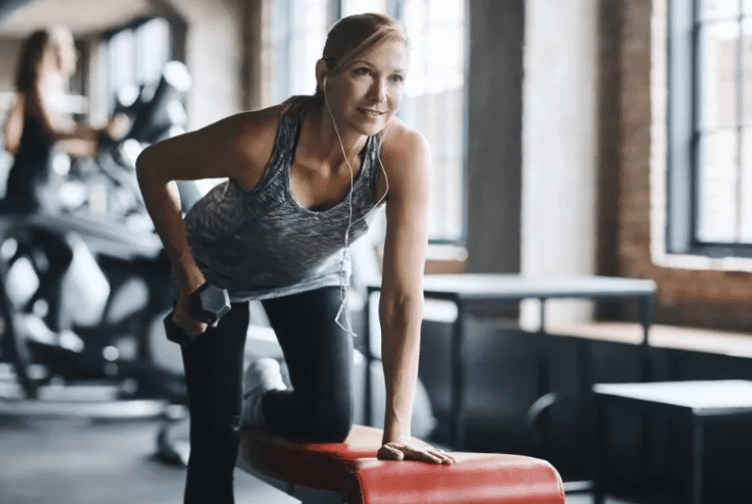 A woman is standing on the bench in a gym
