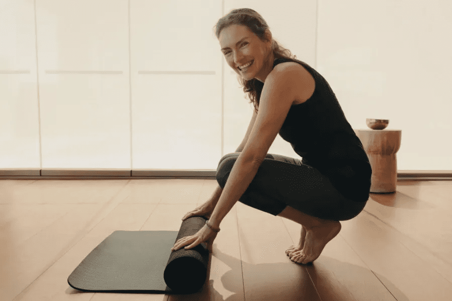 A woman kneeling down on the floor with a yoga mat.