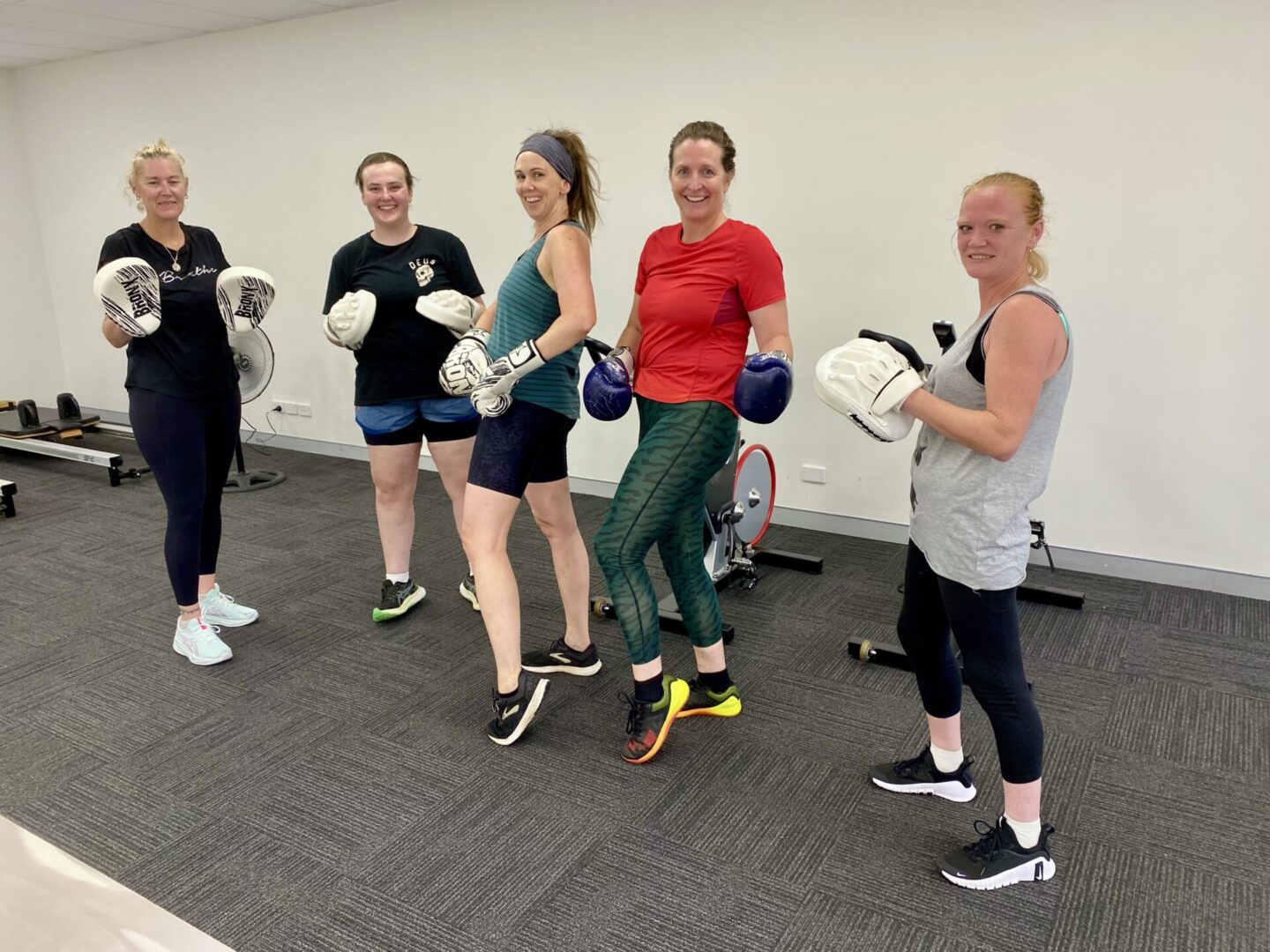A group of women standing in gym with boxing gloves.