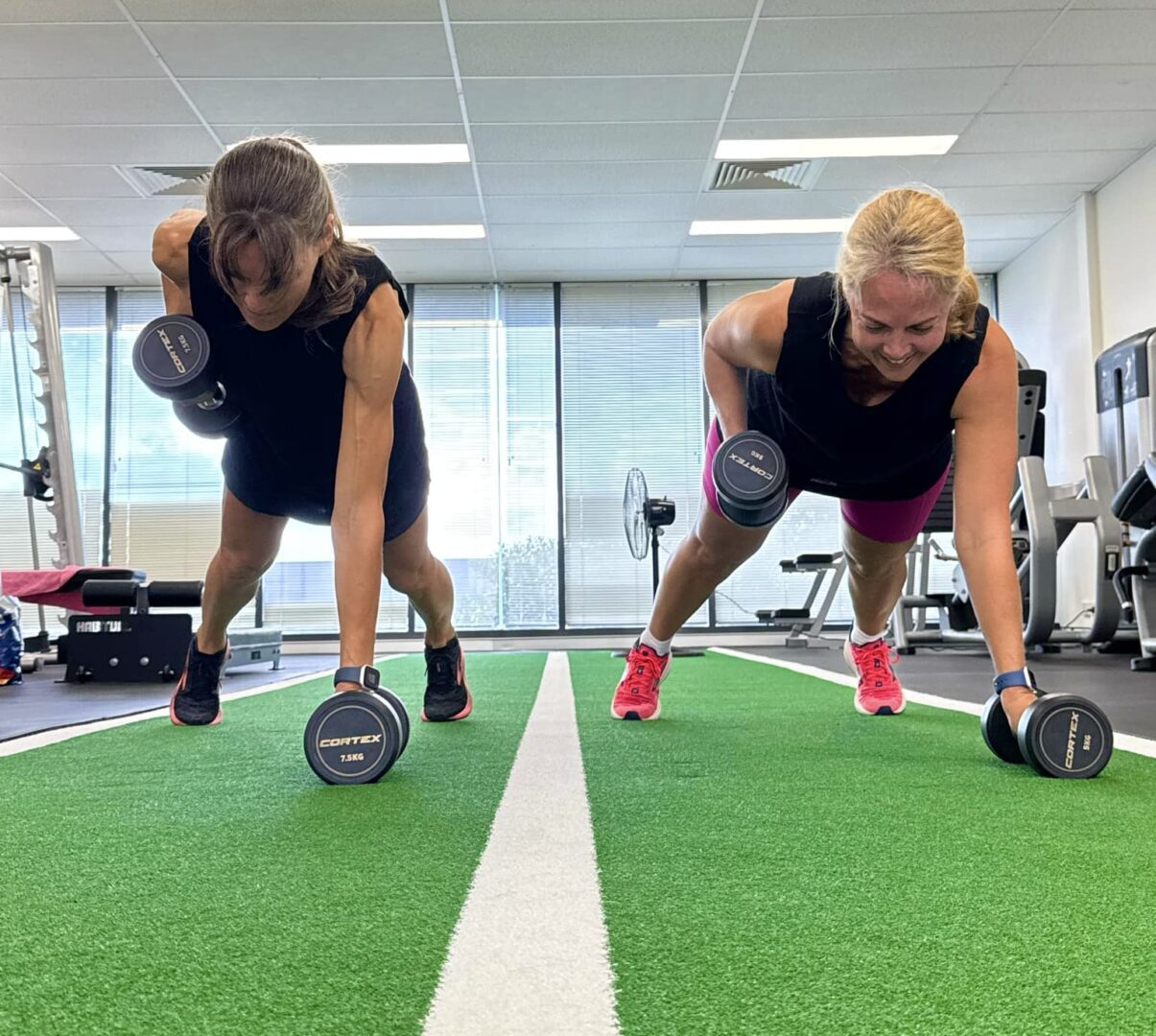 Two women are doing push ups with dumbbells.