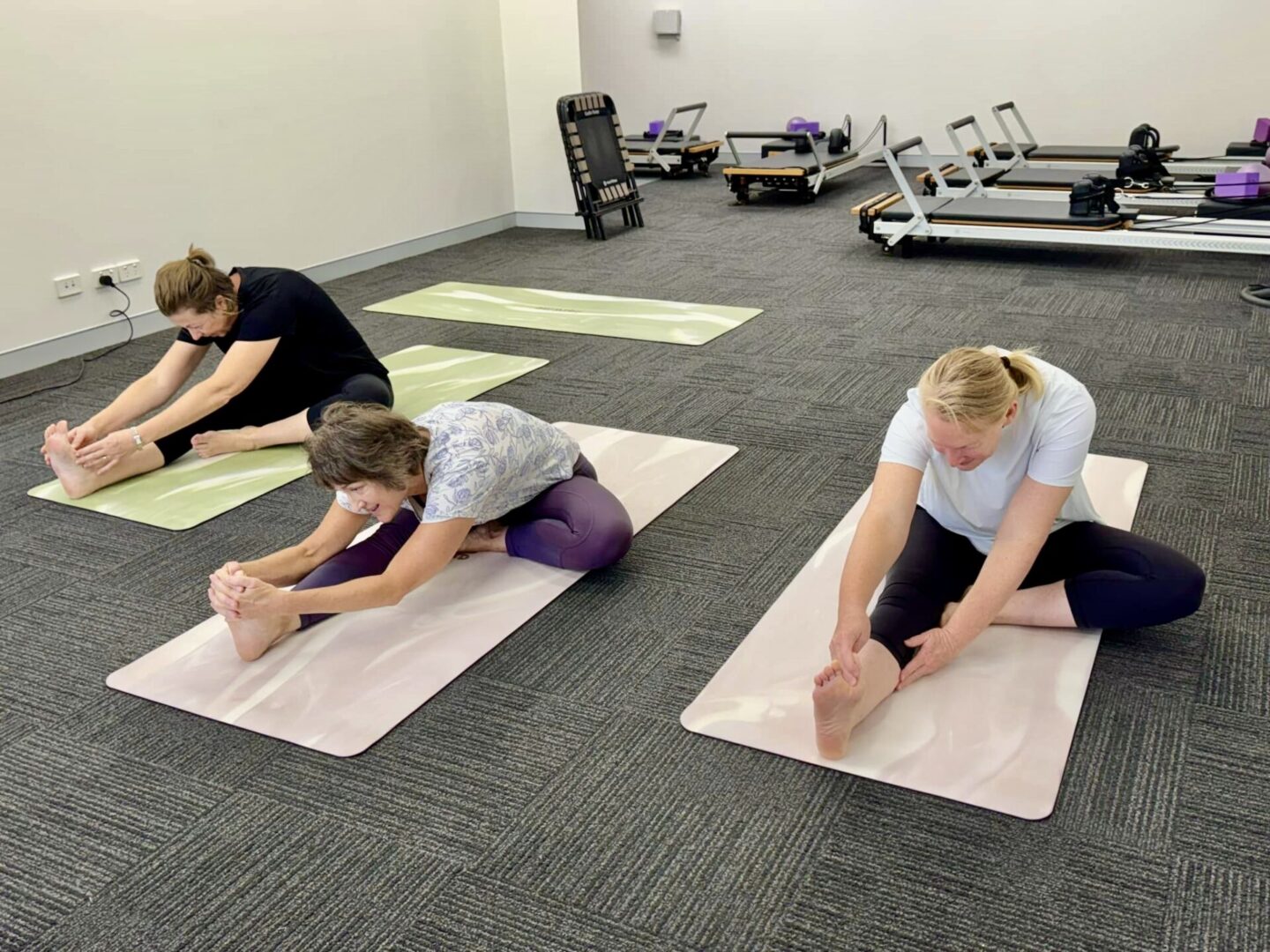 Three people are practicing yoga on mats in a gym.