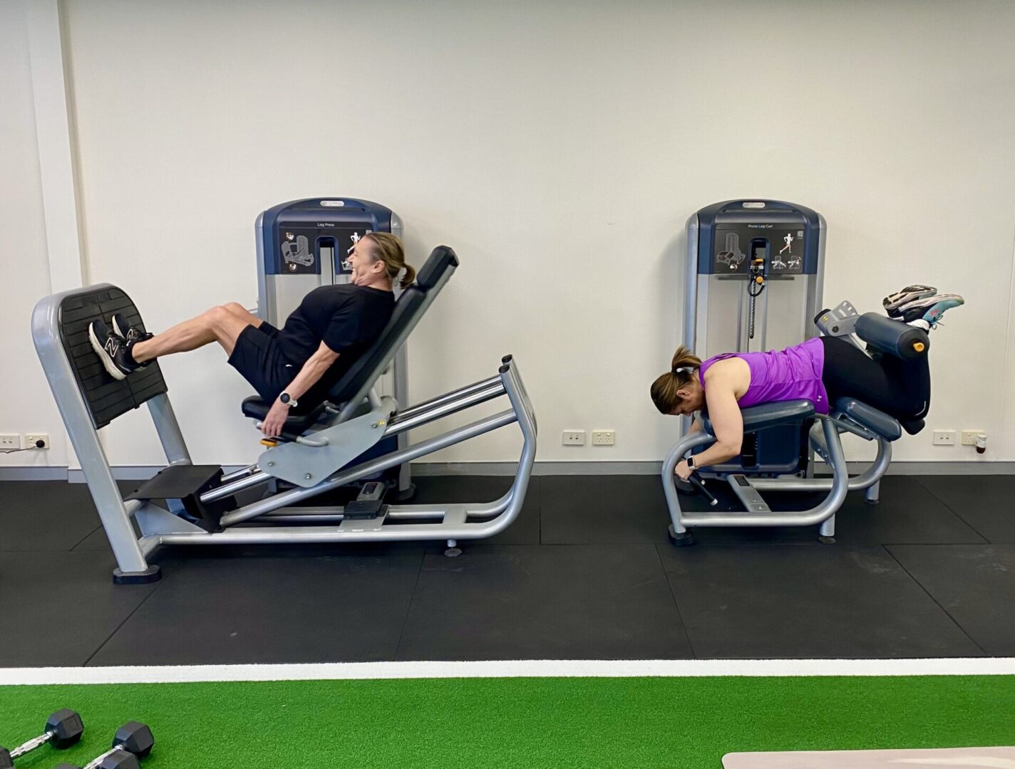 Two people are using a machine to work their legs.